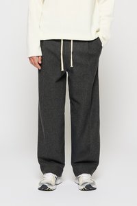 Gray, wide-leg trousers made of textured fabric, featuring a drawstring waist with cream ties. Paired with white and gray athletic shoes.