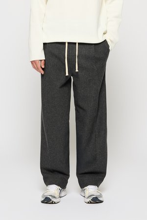 Grijze wijde pantalon van textuurstof, met een tailleband met een trekkoord en crèmekleurige strikken. Gecombineerd met witte en grijze sportschoenen.