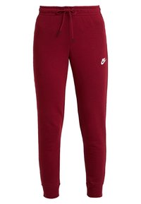 Röda sweatpants i mjukt tyg med resår i midjan och dragsko, avsmalnande ben och en liten vit Nike-logotyp på vänster lår.