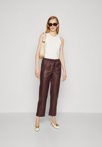 Pantalon en cuir bordeaux avec une taille élastique, associé à un débardeur blanc ajusté et des chaussures à enfiler crème avec des accents dorés.