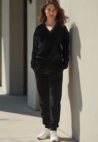 Fekete bolyhos loungewear szett, V-nyakú, hosszú ujjú pulóverrel és hozzá illő szabott jogger nacikkal, fehér tornacipővel párosítva.