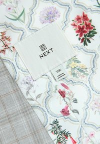 Floral-patterned fabric in white with touches of pink, red, and yellow flowers; textured gray fabric with a checked pattern; includes tag with branding.
