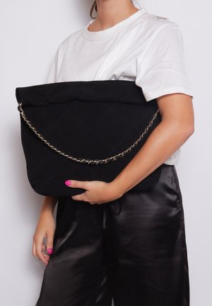 Clutch in tessuto trapuntato nero con tracolla a catena, dotato di una parte superiore ripiegata e una texture liscia, sorretto su uno sfondo bianco.