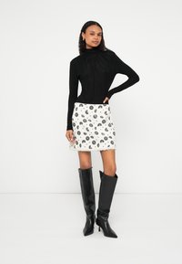 Fekete, hosszú ujjú felső pliszírozott részlettel, fehér mini szoknya fekete virágmintával, és fekete, térdig érő, magas sarkú csizma.