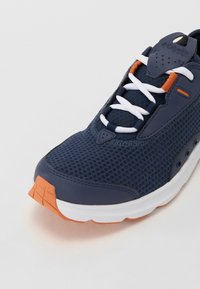 Jūras spēku tīkla sporta apavi ar baltām šņorēm un oranžiem akcentiem; aprīkoti ar mīkstu apkakli, gumijas zoli un elpojošu tekstūru.