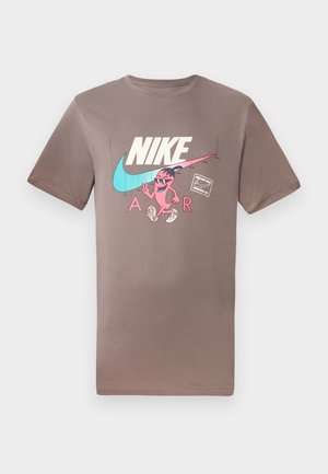 Brūna kokvilnas T-krekls ar krāsainu grafiku, kurā attēlots tēls ar saulesbrillēm, blakus Nike un Air logotipiem kontrastējošās krāsās.
