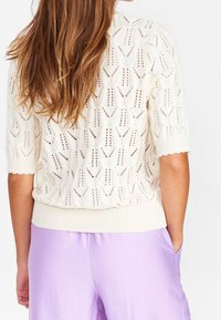 Stickad krämfärgad tröja med korta ärmar, med ett strukturerat mönster och ribbad nederkant. Matchad med lavendel, lätta byxor i satinliknande material.