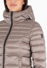 Gewatteerde jas in licht taupe met horizontale quilt, voorzien van een hoge kraag en een ritssluiting aan de voorkant, accenterend met een klein logo op de mouw.