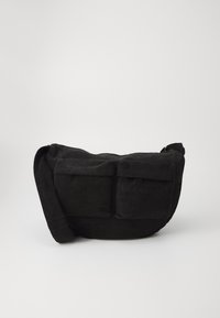 Black corduroy crossbody bag with adjustable strap, featuring front pockets and a soft texture. Compact design with minimal detailing.