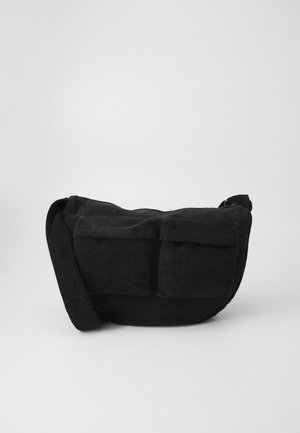 Zwarte corduroy schoudertas met verstelbare strap, voorzien van voorzakken en een zachte textuur. Compact ontwerp met minimale details.
