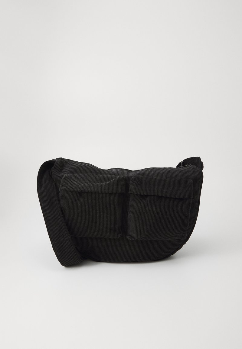 Black corduroy crossbody bag with adjustable strap, featuring front pockets and a soft texture. Compact design with minimal detailing.