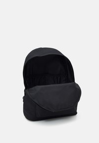 Sort rygsæk med blødt stofudvendig, afrundet top, stor åben rum og klaplukning. Minimalistisk design, ingen synlige hardware.