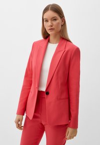 Blazer rose corail avec un bouton noir unique, revers cranté et deux poches avant. Assorti à un top blanc à col ras du cou. Texture lisse.