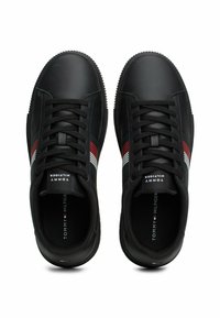 Een paar zwarte sneakers van Tommy Hilfiger met rode, witte en blauwe strepen aan de zijkanten, zwarte veters en een merkgebonden tong.