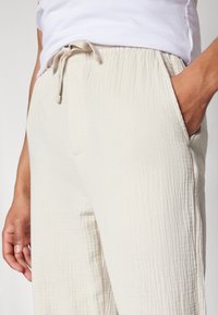 Lichtbeige textuurbroek met een elastische tailleband en koord, voorzien van zijzakken en een losse pasvorm.