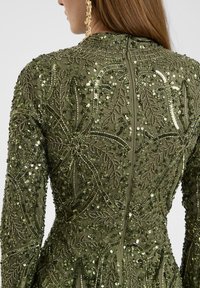 Abito verde di paillettes con intricate fantasie a foglia, tessuto opaco e silhouette aderente con scollo alto e maniche lunghe.