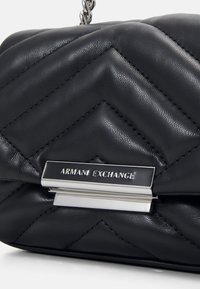 Černá prošívaná kožená kabelka s šikmým vzorem, stříbrným kováním a kovovým štítkem s vyrytým nápisem "ARMANI EXCHANGE."