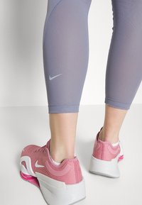 Scarpe Nike rosa con suole e dettagli bianchi, abbinate a pantaloni capri grigi con un piccolo logo bianco e un tessuto liscio e strutturato.