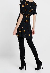 Svart blommig klänning med orange-gula blommor, korta puffärmar och utsvängd nederdel. Matchad med höga svarta mockastövlar och klackar.