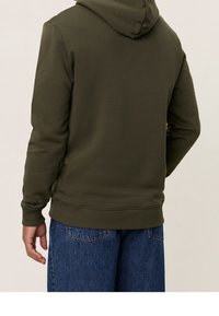 Mörkgrön hoodie med dragsko i huven, ribbad fåll och manschetter, kombinerad med blå jeans. Tillverkad av mjukt, strukturerat tyg.