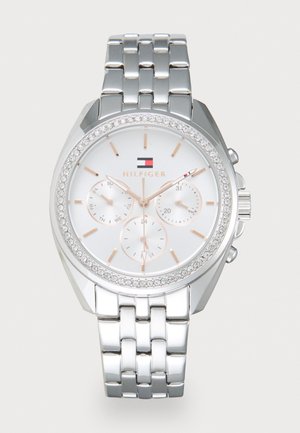 Montre en métal argenté avec un grand cadran rond, un cadran blanc, des accents en or rose, trois sous-cadrans et une lunette incrustée de cristaux. Les chaînes sont polies.