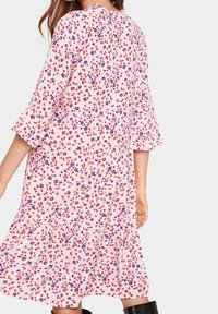 Šaty s květinovým potiskem na růžovém pozadí, s širokými rukávy, vrstvenou sukní a malými vzory červených, fialových a modrých květin.