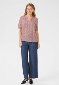 Blouse à manches courtes avec un motif rouge et blanc, décolleté en V, assortie à un pantalon en denim bleu à jambes larges et des escarpins noirs à bout pointu.