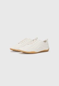 Des chaussures de sport blanches avec un dessus synthétique lisse, dotées de lacets, d'accents latéraux et d'une semelle en caoutchouc gum. Bout arrondi, design minimaliste.