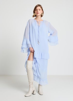Robe en chiffon bleu clair avec manches évasées et ourlet à volants, dotée d'une fente à l'avant. Complétée par des bottes blanches montantes jusqu'aux genoux.