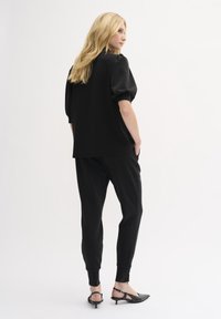 Čierny voľný top s krátkym rukávom v nadmernej veľkosti skombinovaný s čiernymi zúženými teplákmi. Materiál sa zdá byť jemný; top má voľný strih. Obuv: čierne sandále na nízkom podpätku.