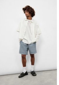 Trumpomis rankovėmis, šviesios spalvos marškiniai su sagomis, dėvimi ant baltos spalvos marškinėlių, derinami su pilkomis šortais. Aksesuarai: balti kojinės ir juodi batai.