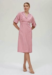 Sarkanbalts svītrains kleita ar apkakles kakla izgriezumu, īsām piedurknēm, piegulošu vidukli un pogu akcentiem. Gluda auduma ar ceļa garuma griezumu.