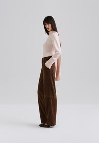 Light pink ribbed long-sleeve top paired with brown suede wide-leg pants, featuring pockets and a smooth texture.