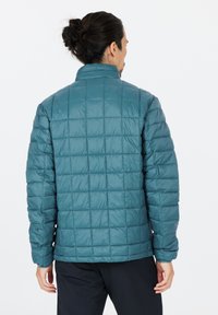 Teal quiltet pufferjakke med ståkrave, lange ærmer og en tekstureret overflade med syntede kvadratmønstre. Bagfra set.