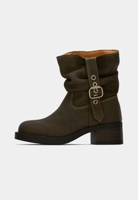 Bottines en cuir vert olive avec une tige fléchie, accent de boucle en argent et un talon block moyen. Détails de couture le long des bords.