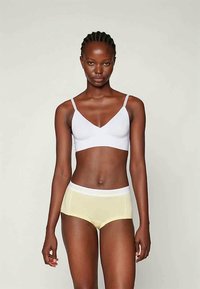 Hvit bralette med tynne stropper, kombinert med lysegule boyshorts som har hvit elastisk midjebånd, glatt stoff og enkelt design.