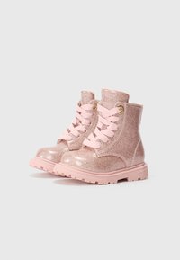 Rosa glittriga ankelskor med en kraftig sula, som har rosa snören och gyllene öglor. Slät textur med en glänsande finish.