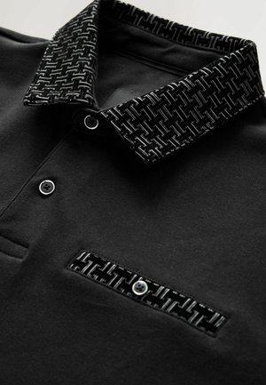 Polo shirt nera con colletto a motivo texturizzato, chiusura a bottoni e taschino con design simile. Tessuto liscio con dettagli strutturati.
