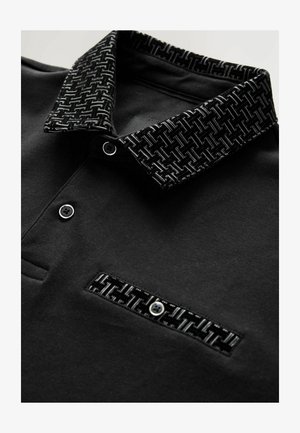 Polo shirt nera con colletto a motivo texturizzato, chiusura a bottoni e taschino con design simile. Tessuto liscio con dettagli strutturati.