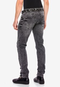 Graue Denim-Jeans mit schmalem Schnitt, die ein strukturiertes Muster, Gesäßtaschen und einen schwarzen Nieten-Gürtel für zusätzliche Details aufweisen.