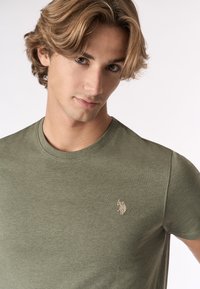 T-shirt verde oliva in morbido cotone con colletto rotondo e maniche corte. Presenta un piccolo logo ricamato sulla parte sinistra del petto.