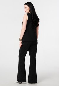 Zwarte mouwloze top gecombineerd met zwarte wijde broek met een subtiele glans. Soepele textuur met een getailleerde pasvorm, die de silhouet benadrukt.