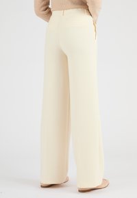 Pantaloni a gamba larga in morbido tessuto crema, caratterizzati da un design pulito, vita alta e tasche posteriori. Texture liscia con un leggero lucido.