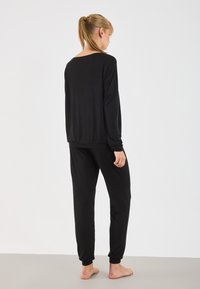 Crni loungewear komplet koji se sastoji od majice dugih rukava i tapered hlača, oboje od mekog materijala, s opuštenim krojem i rebrastim manžetama.