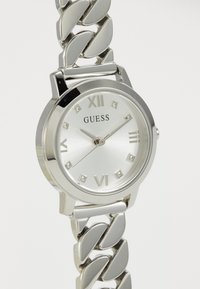 Reloj de acero inoxidable plateado con una esfera redonda, números romanos y un dial texturizado. La correa presenta un diseño de eslabones de cadena.