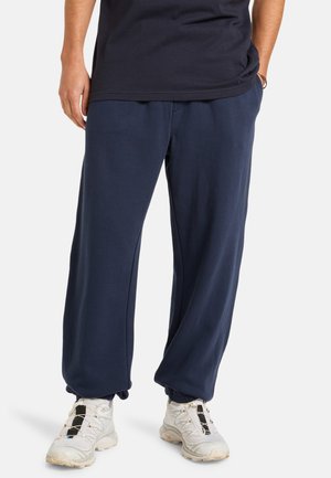 Navy blue sweatpants made of soft fabric, featuring a loose fit and elastic waistband. Pairing with white athletic shoes.
