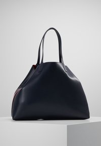 Duża granatowa skórzana torba typu tote z dwoma uchwytami, o zaokrąglonym kształcie i delikatnym połysku. Posiada kontrastowe czerwone wnętrze oraz stonowany design.