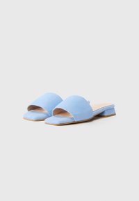 Mule aperti in suede blu con punta rotonda, suola piatta e tacco a blocco piccolo, caratterizzati da una texture liscia e da un design minimalista.
