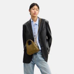 Kobieta nosząca oversize czarny skórzany blezer, jasnoniebieską koszulę, luźne dżinsy, nosi małą oliwkowozieloną torebkę z złotym łańcuszkiem.