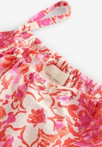 Kvetinová tkanina s odtieňmi ružovej a červenej, s nariasenou elastickou časťou na vrchu a závesnou slučkou. Viditeľná značka výrobcu.